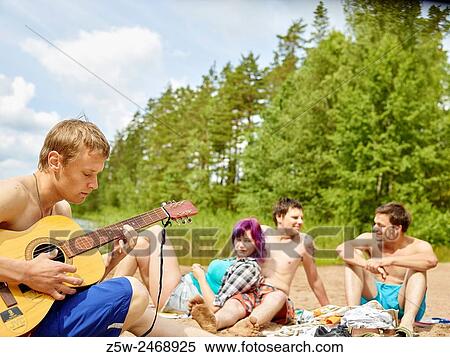 Stock Photography - The group of the friends chilling out on the beach, summer day. Shot in southern Finland.. Fotosearch