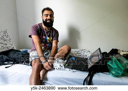 Tilburg, Netherlands. Brazilian male traveller sitting on the bed of his Airbnb guest room with his laptop computer at arms length. View Large Photo Image Stock Image - Tilburg, Netherlands. Brazilian male traveller sitting on the bed of his Airbnb guest room with his laptop computer at arms length.. Fotosearch