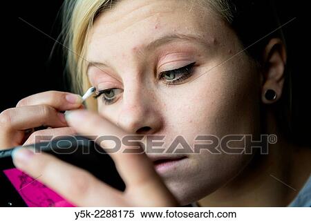 Tilburg, Netherlands. Close up of a young, blonde woman, applying make up to her eyes, while using her smart phone as a mirror. View Large Photo Image Stock Photography - Tilburg, Netherlands. Close up of a young, blonde woman, applying make up to her eyes, while using her smart phone as a mirror.. Fotosearch