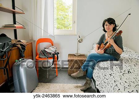 Tilburg, Netherlands. Female Italian violinist sitting on the bed of her Airbnb guest room, while practising with her violin. View Large Photo Image Stock Photography - Tilburg, Netherlands. Female Italian violinist sitting on the bed of her Airbnb guest room, while practising with her violin.. Fotosearch
