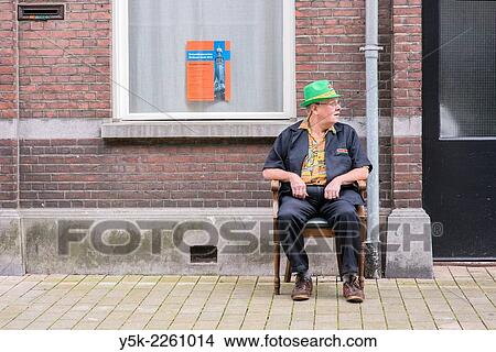 Tilburg, Netherlands. Man sitting in his newly bought chair in front of a facade in the streets. View Large Photo Image Picture - Tilburg, Netherlands. Man sitting in his newly bought chair in front of a facade in the streets.. Fotosearch