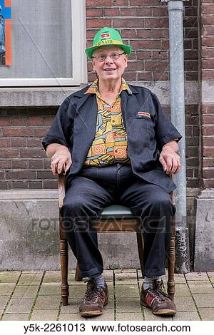 Tilburg, Netherlands. Man sitting in his newly bought chair in front of a facade in the streets. View Large Photo Image Stock Image - Tilburg, Netherlands. Man sitting in his newly bought chair in front of a facade in the streets.. Fotosearch