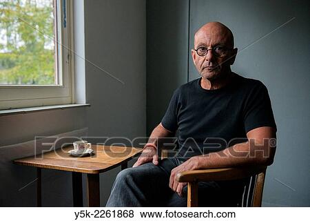 Tilburg, Netherlands. Portrait of a bald man wearing glasses, drinking a cup of coffee while sitting at a small table near the window. View Large Photo Image Stock Photo - Tilburg, Netherlands. Portrait of a bald man wearing glasses, drinking a cup of coffee while sitting at a small table near the window.. Fotosearch