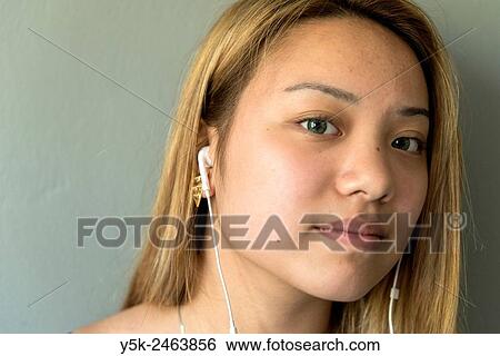 Tilburg, Netherlands. Studio portrait of a young Chinese girl with headphones, listening to the music on her smartphone, while standing in front of a grey background. View Large Photo Image Stock Photograph - Tilburg, Netherlands. Studio portrait of a young Chinese girl with headphones, listening to the music on her smartphone, while standing in front of a grey background.. Fotosearch