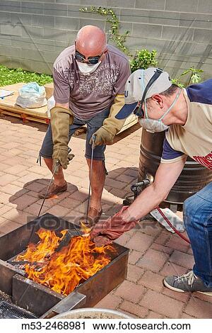 Stock Image - Two man handle raku ceramic objects after the heating process. Bovisio Masciago. Province of Monza and Brianza. Lombardy. Italy.. Fotosearch