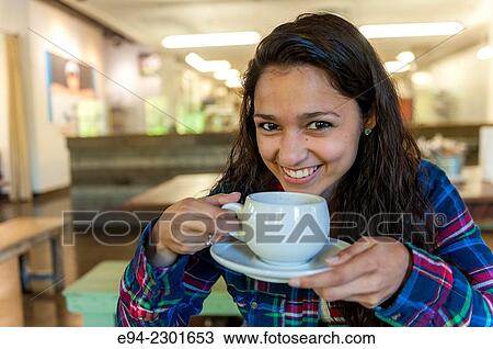 Stock Image - 19 year old brunette woman holding a coffee cup in a restaurant.. Fotosearch