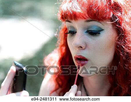 A 23 year old red head woman applying lip gloss while looking at cell phone. View Large Photo Image Stock Image - A 23 year old red head woman applying lip gloss while looking at cell phone.. Fotosearch