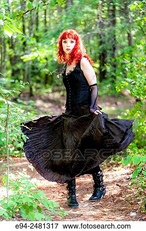 A 23 year old red head woman in a long black dress, looking at the camera and walking on a path in a forest setting. View Large Photo Image Stock Photo - A 23 year old red head woman in a long black dress, looking at the camera and walking on a path in a forest setting.. Fotosearch