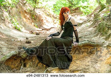 A 23 year old red head woman looking at the camera in a long black dress, sitting on a path in a forest setting. View Large Photo Image Stock Image - A 23 year old red head woman looking at the camera in a long black dress, sitting on a path in a forest setting.. Fotosearch