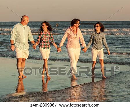 A family, Mom, Dad and twin daughters walk, holding hands, in the surf at the beach. Coastal Georgia, USA View Large Photo Image Stock Photo - A family, Mom, Dad and twin daughters walk, holding hands, in the surf at the beach. Coastal Georgia, USA. Fotosearch