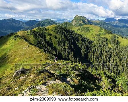Stock Image - A hiker follows a path on the crest of a bald mountain in Alaska, USA. More of the mountain range can be seen in the distance.. Fotosearch