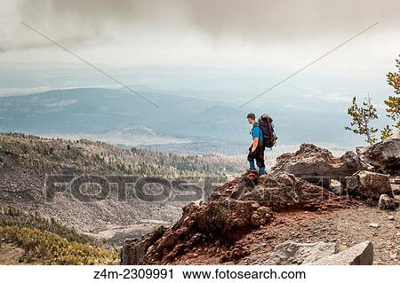A male backpacker stands at the edge of a cliff looking out over other mountains in the distance. Mount Adams, Washington, USA. View Large Photo Image Stock Image - A male backpacker stands at the edge of a cliff looking out over other mountains in the distance. Mount Adams, Washington, USA.. Fotosearch
