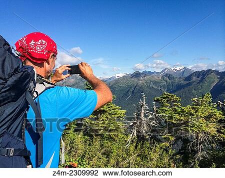 A male backpacker uses a smartphone to take a photo of a distant mountain range in Alaska, USA. View Large Photo Image Stock Image - A male backpacker uses a smartphone to take a photo of a distant mountain range in Alaska, USA.. Fotosearch