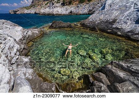 Stock Photo - A man relaxing on the water of a natural pool with sea water. Trachila village, Messenia, Greece.. Fotosearch