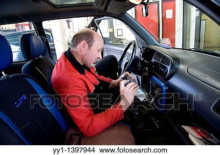 A mechanic installs a new cd-player in the dasboard of one of his cutomers car. View Large Photo Image Picture - A mechanic installs a new cd-player in the dasboard of one of his cutomers car.. Fotosearch