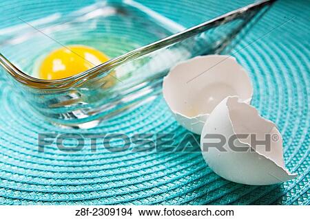 A raw egg is placed in a bowl for mixing together potato pancakes while the broken eggshell is placed nearby. View Large Photo Image Picture - A raw egg is placed in a bowl for mixing together potato pancakes while the broken eggshell is placed nearby.. Fotosearch