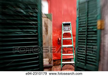 Stock Photo - A step ladder resting against a red wall in a back yard with green shutters by the entrance, Alabama USA.. Fotosearch