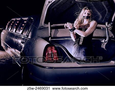 Stock Image - Attractive blond girl inside the trunk of the limousine, hands tied and mouth taped, intentional noise added.. Fotosearch