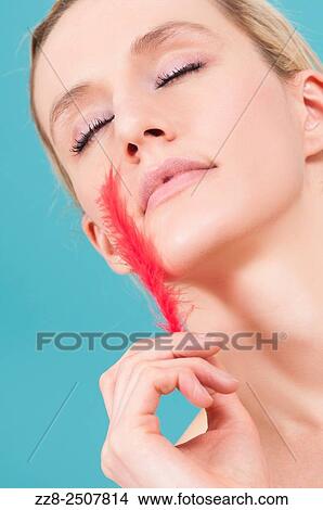 Beautiful young Caucasian woman feeling face with a red fether. View Large Photo Image Picture - Beautiful young Caucasian woman feeling face with a red fether.. Fotosearch