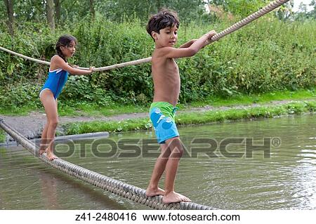 Children dressed in swimming suits balancing on a rope above water. View Large Photo Image Stock Photograph - Children dressed in swimming suits balancing on a rope above water.. Fotosearch