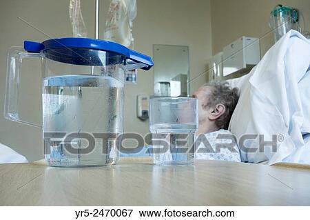 Stock Photo - Elderly lady in her nineties in bed on NHS hospital ward with jug of water on bedside table. England, United Kingdom.. Fotosearch