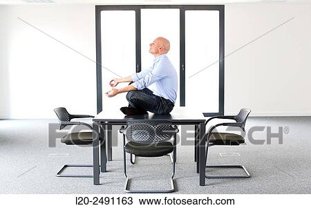 Stock Image - Executive doing Yoga. Empty office. Meeting room.. Fotosearch