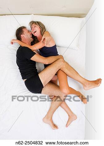 Stock Image - Happy couple smiling and hugging on the bed top view.. Fotosearch