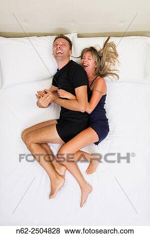 Stock Photo - Happy couple smiling and hugging on the bed top view.. Fotosearch