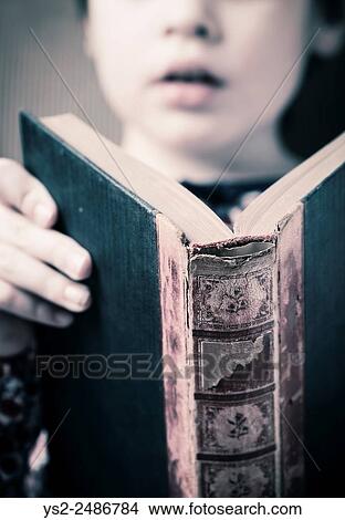 Picture - Little girl reading in an old book. Conceptual image of intelligence and learning to read at a young age.. Fotosearch