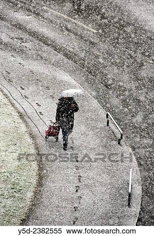Stock Photography - lonely woman walkinh with umbrella and shopping bag in heavy snowfall, Geneva, Switzerland.. Fotosearch