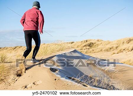 Stock Image - Man jogging on frost coverd dunes on Seaton Carew beach, north east England, United Kingdom.. Fotosearch