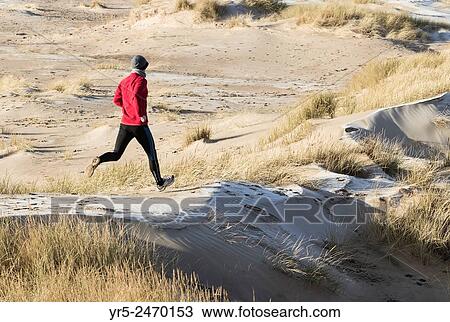 Stock Image - Man jogging on frost coverd dunes on Seaton Carew beach, north east England, United Kingdom.. Fotosearch