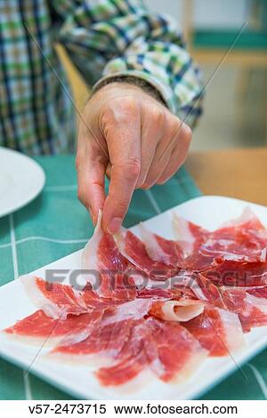Stock Photography - Man's hand having Iberian ham. Close view.. Fotosearch