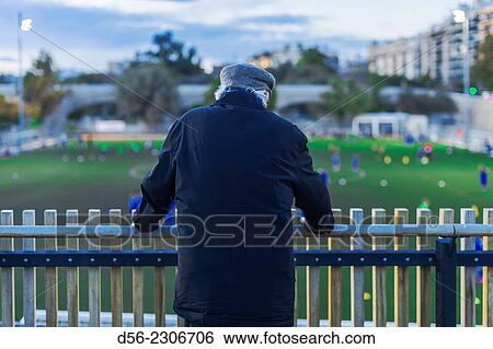 Stock Photograph - Old man watching a football field in the river bed Turia, Valencia, Spain.. Fotosearch