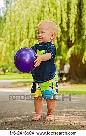 One year old boy, standing barefoot in a park, holding purple plastic ball. View Large Photo Image Picture - One year old boy, standing barefoot in a park, holding purple plastic ball.. Fotosearch