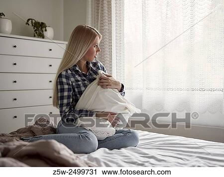 Stock Image - Pensive young woman sits on the bed, sad feelings.. Fotosearch