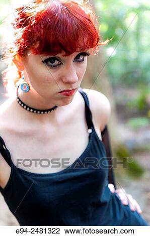 Stock Image - Portrait of a 23 year old red head woman looking at the camera with an angry expression, outdoors.. Fotosearch