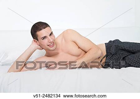 Picture - Portrait of a man laying in bed smiling at camera. Fotosearch