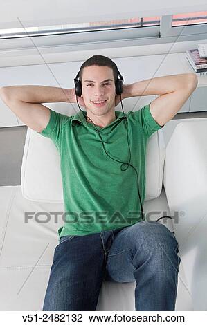 Stock Image - Portrait of a man lying on the sofa listening to music with headphones. Fotosearch