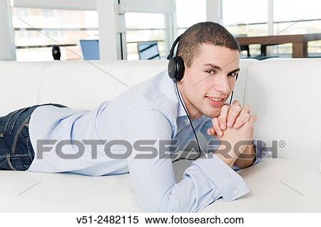 Portrait of a man lying on the sofa listening to music with headphones View Large Photo Image Stock Photography - Portrait of a man lying on the sofa listening to music with headphones. Fotosearch