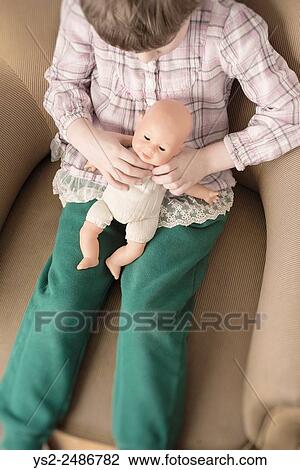 Portrait of little girl holding plastic doll in her hands. She is sitting in an armchair. View Large Photo Image Stock Image - Portrait of little girl holding plastic doll in her hands. She is sitting in an armchair.. Fotosearch