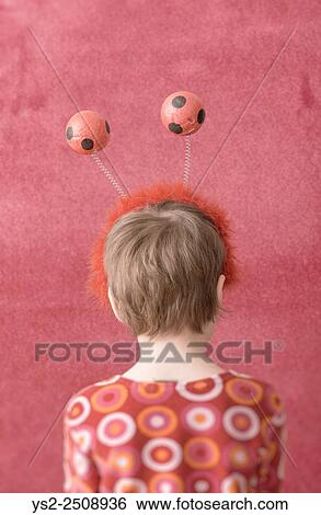 Stock Photograph - Portrait of little girl wearing fun headband with balls. She is turned away from the camera showing her back.. Fotosearch