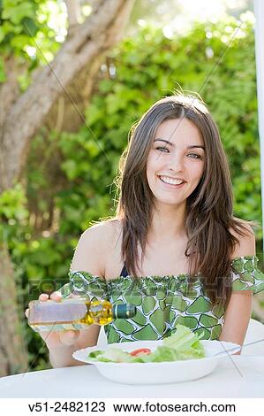 Stock Image - Pretty woman enjoying a salad with olive oil outdoors smiling at camera. Fotosearch
