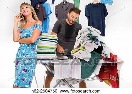 Stock Image - She is happily phoning while a man very sweaty ironing many clothing.. Fotosearch