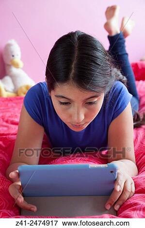 Teenage girl llying on her bed and looking at her digital tablet. View Large Photo Image Stock Photo - Teenage girl llying on her bed and looking at her digital tablet.. Fotosearch