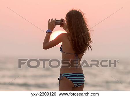 Stock Image - Teenager at the beach taking a photo of the sunset. Tarifa, Cadiz, Costa de la Luz, Andalusia, Spain.. Fotosearch