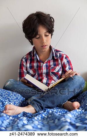 Ten year old boy reading a book sitting on his bed. View Large Photo Image Stock Photo - Ten year old boy reading a book sitting on his bed.. Fotosearch