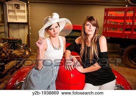 Two female models sitting on antique red automobile talking and whispering View Large Photo Image Stock Photo - Two female models sitting on antique red automobile talking and whispering. Fotosearch
