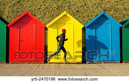 Stock Photograph - Whitby, North Yorkshire, England, United Kingdom. Europe. Mature jogger passing beach huts on Whitby beach just after sunrise.. Fotosearch