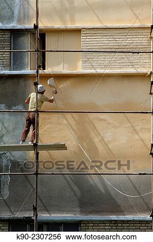 Stock Photograph - Worker standing of a scaffolding and painting the wall of a building, Tehran, Iran, Asia.. Fotosearch